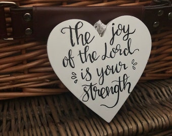White wooden hanging heart with The joy of the Lord is your strength handlettered in black. 10cm high.