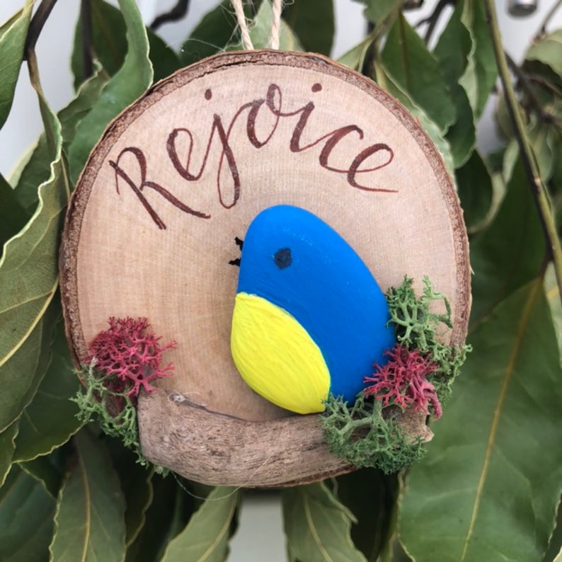 Hanging Ornament Rejoice Pebble Bird on a driftwood branch mounted onto a log slice.