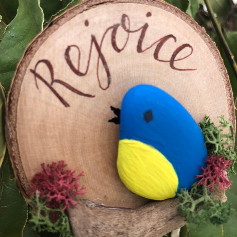 Hanging Ornament Rejoice Pebble Bird on a driftwood branch mounted onto a log slice.
