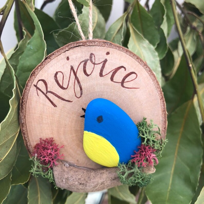 Hanging Ornament Rejoice Pebble Bird on a driftwood branch mounted onto a log slice.