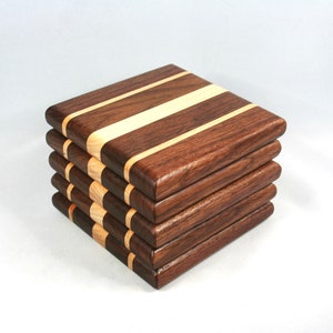May include: A stack of five square wooden coasters. Each coaster is made of dark brown wood with a light-colored wood stripe running across the center. The coasters are stacked neatly on a white background.