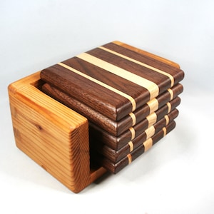 May include: A set of wooden coasters with a holder. The coasters are made of dark brown and light wood strips. The holder is made of light-colored wood. The coasters are stacked neatly inside the holder.