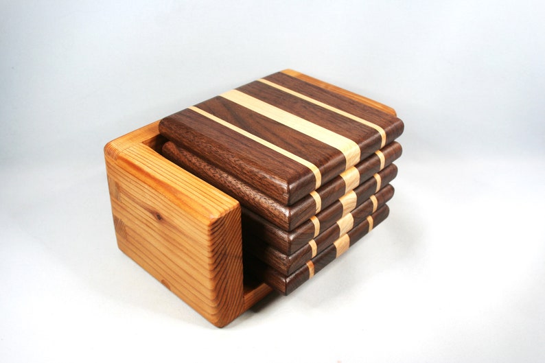 May include: A set of wooden coasters with a holder. The coasters are made of dark brown and light wood strips. The holder is made of light-colored wood. The coasters are stacked neatly inside the holder.