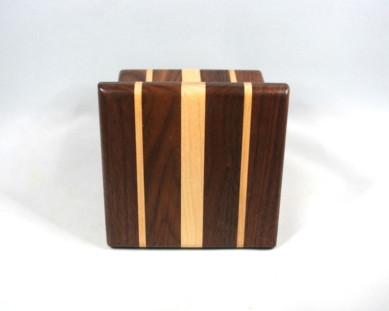 May include: A wooden block with a rectangular shape. The block features a vertical design with alternating stripes of dark brown and light tan wood. The wood grain is visible, and the block has a smooth, polished finish.