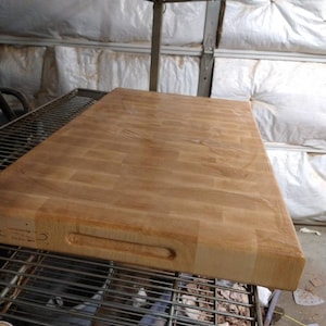 May include: A large, rectangular, wooden cutting board with a checkered pattern. The board has a single handle and is made of light brown wood.