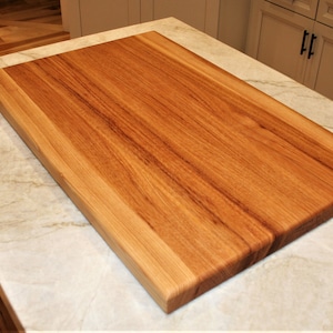 May include: A rectangular wooden cutting board with a light brown finish. The board is made of wood and has a smooth surface. The cutting board is approximately 24 inches long and 18 inches wide. Kitchenware.