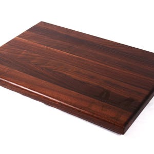May include: A rectangular, dark brown wooden cutting board with a smooth, polished surface. The wood grain is visible, and the edges are slightly rounded. This kitchen item is ideal for food preparation.