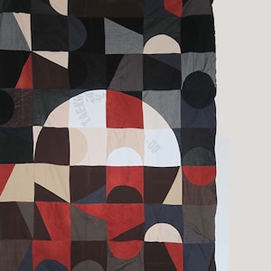 Könnte beinhalten: Ein geometrischer Patchwork-Deckenbezug mit einer Vielzahl von Farben und Formen, darunter Rot, Schwarz, Weiß und Braun. Die Decke besteht aus verschiedenen Stoffen und Texturen und hat ein modernes und abstraktes Design.