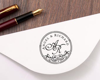 Könnte beinhalten: Ein weißer Umschlag mit einem schwarzen und weißen runden Stempel. Der Stempel zeigt den Text "Angel & Richard" und die Initialen "A & R" in einer dekorativen Schreibschrift.