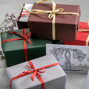 May include: Several wrapped gift boxes in shades of red, green, and grey. Each box is tied with a contrasting ribbon, some with natural raffia bows. A greeting card with a tree design is also visible, suggesting a gift-giving theme.