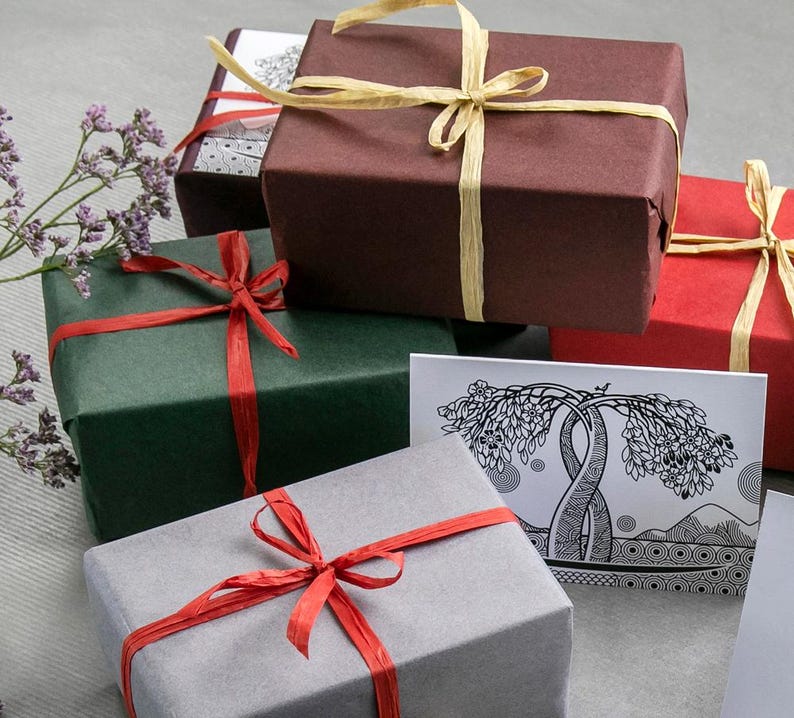 May include: Several wrapped gift boxes in shades of red, green, and grey. Each box is tied with a contrasting ribbon, some with natural raffia bows. A greeting card with a tree design is also visible, suggesting a gift-giving theme.