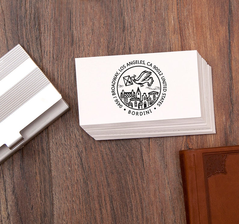 May include: A stack of white business cards with a black circular design featuring a flying bird carrying an envelope, buildings, and the text "BORDINI". The cards are on a wooden surface, next to a silver card holder.