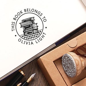 May include: A black and white stamp with a stack of books and the text "This book belongs to Olivia Light". The stamp is in a brown box with a brown ribbon.