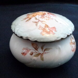 May include: A white porcelain jar with a lid, decorated with a floral pattern in shades of orange, pink, and green.