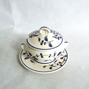 Puede incluir: Una sopera de cerámica blanca con un diseño floral azul y blanco. La sopera tiene una tapa y un platillo a juego.