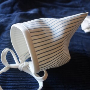 May include: A white bonnet with blue stripes and a white tie. The bonnet is made of a soft, lightweight fabric and is perfect for a baby.