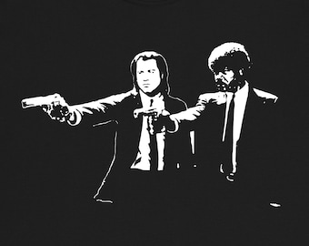 May include: Black t-shirt featuring a white silhouette of two men pointing guns at the viewer. The men are wearing suits and ties.
