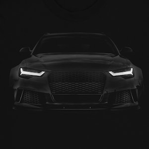 May include: Black t-shirt featuring a silhouette of a black car's front end. The car has a black grille and white headlights.