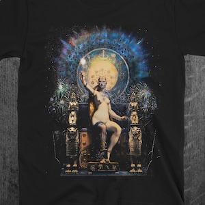 Op de afbeelding: Een zwart T-shirt met een kleurrijke grafische print van een vrouw die op een troon zit. De vrouw houdt een fakkel vast en wordt omringd door een gloeiende halo. De achtergrond is een donkerblauwe en paarse nevel.