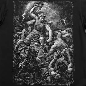 Peut inclure: T-shirt noir avec une illustration détaillée en niveaux de gris représentant un dieu nordique avec un marteau dans une scène de bataille. Le motif comprend des personnages, des éclairs et une chèvre, créant un thème dramatique et mythologique.