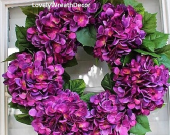 May include: A purple hydrangea wreath with green leaves. The wreath is made of silk flowers and is ideal for a spring or summer door decoration.