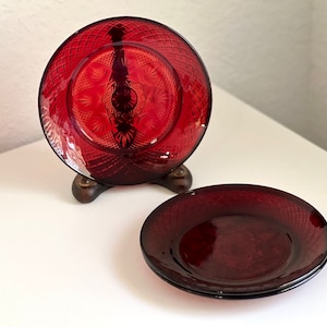 Puede incluir: Dos juegos de platos de vidrio rojo con un patrón de diamante. El juego superior está en un soporte de madera.