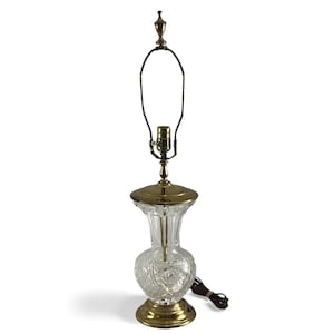 Könnte beinhalten: Eine Vintage-Tischlampe mit einem klaren, geschliffenen Glasfuß in Vasenform und Messingakzenten. Die Lampe hat ein dekoratives Muster auf dem Glas und einen Messingaufsatz und -fuß. Die Lampe ist etwa 46 cm hoch.