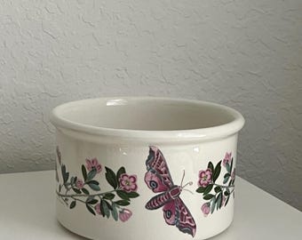 May include: A white ceramic bowl with a floral design featuring pink flowers and a butterfly. The bowl has a rounded shape and a smooth, glossy finish.