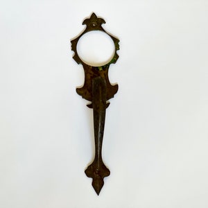 May include: Ornate antique door handle with a decorative design and a long, pointed handle. The handle is made of metal and has a dark brown finish.