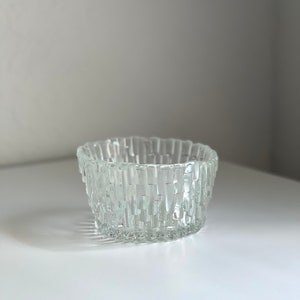 May include: A clear glass bowl with a textured, geometric design. The bowl is round and has a wide rim.
