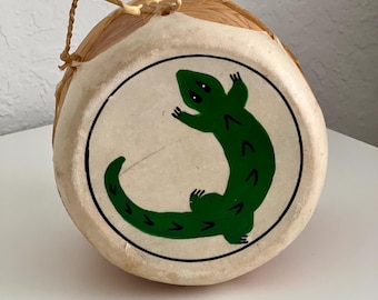 May include: A small, round, wooden drum with a leather head. The drum has a green lizard painted on the front. The drum has a leather strap for carrying.
