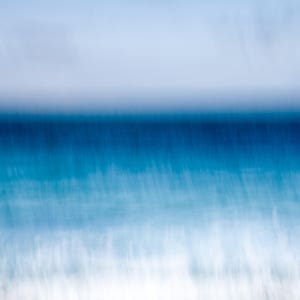 May include: A blurred abstract image of the ocean with a blue sky above. The water is a light blue colour and the sky is a light grey colour.