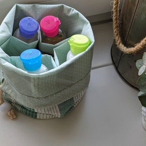 May include: A green and white polka dot fabric pouch with a drawstring closure. The pouch contains four small bottles with colorful lids. The bottles are filled with liquid.
