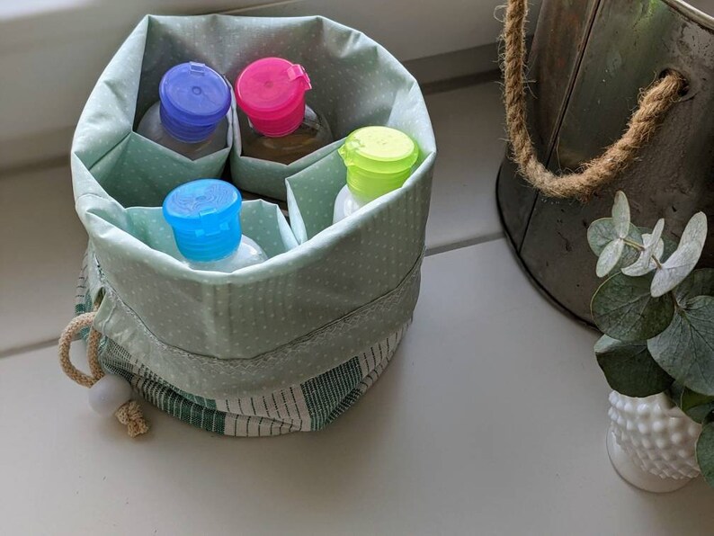 May include: A green and white polka dot fabric pouch with a drawstring closure. The pouch contains four small bottles with colorful lids. The bottles are filled with liquid.