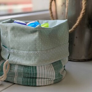 May include: A green and white striped fabric drawstring bag with a green polka dot top. The bag is filled with colorful plastic toys.
