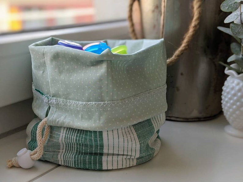 May include: A green and white striped fabric drawstring bag with a green polka dot top. The bag is filled with colorful plastic toys.