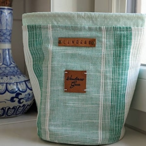 May include: Green and white striped fabric storage bin with a brown leather label that says "Wanderess Gear" and a smaller brown leather label that says "LINDSAY".