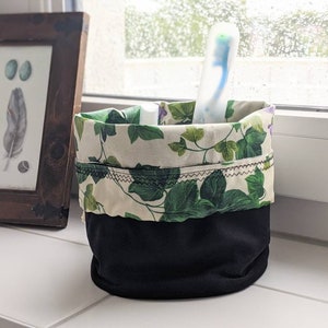 May include: A black and white fabric storage container with a green and white floral pattern. The container is filled with a toothbrush.