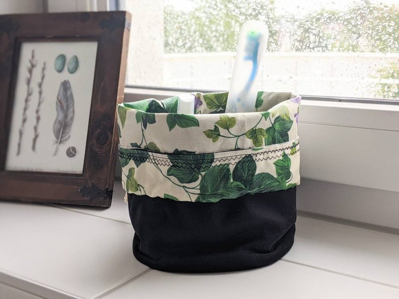 May include: A black and white fabric storage container with a green and white floral pattern. The container is filled with a toothbrush.