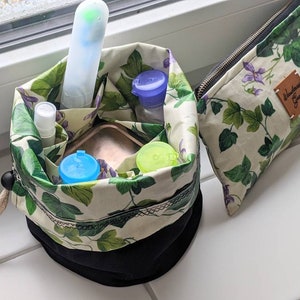 May include: A black and white drawstring bag with a green and white floral pattern. The bag is filled with various small containers and a white tube. The bag is sitting on a white surface. The bag has a label that says "Wanderlust Girl".