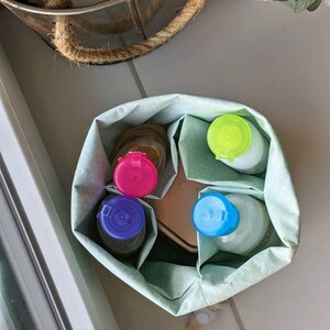 May include: A green fabric storage bag with white polka dots, containing four bottles with different colored lids: blue, pink, green, and light blue. The bottles are labeled "Conditioner".