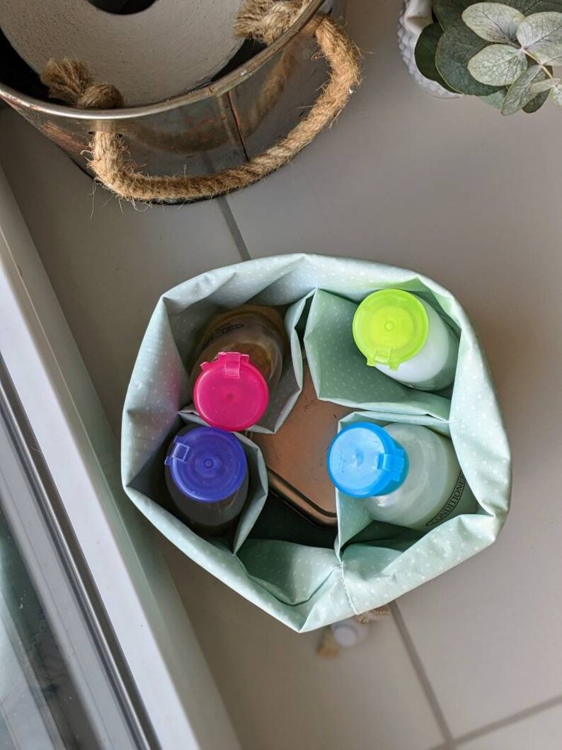 May include: A green fabric storage bag with white polka dots, containing four bottles with different colored lids: blue, pink, green, and light blue. The bottles are labeled "Conditioner".