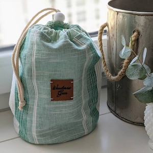 May include: Green and white striped drawstring bag with a brown leather tag that says "Wanderlust Goods".