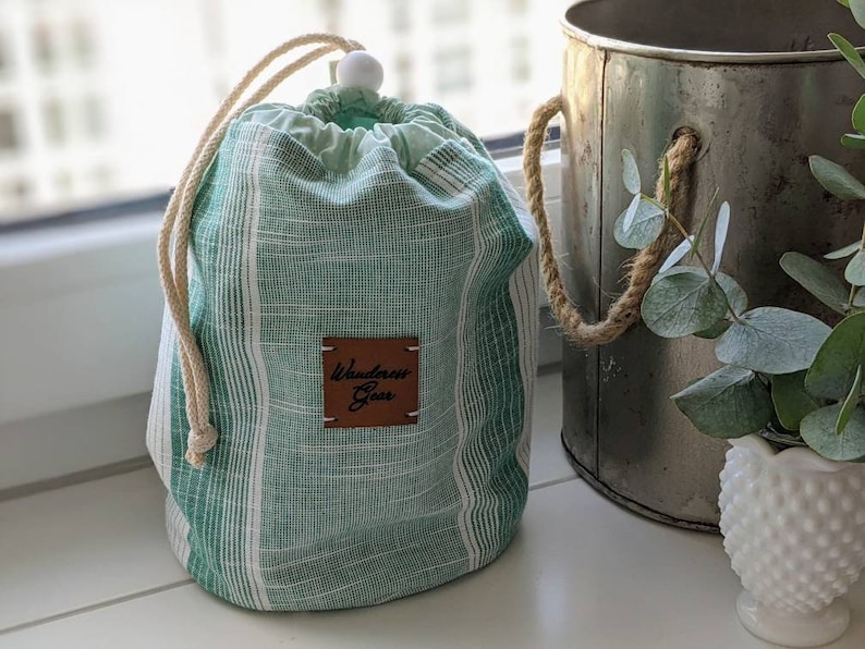 May include: Green and white striped drawstring bag with a brown leather tag that says "Wanderlust Goods".