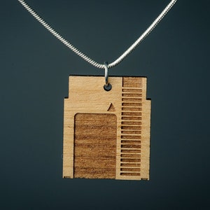 Könnte beinhalten: Ein Holzanhänger in Form einer alten Videospielkassette hängt an einer silbernen Kette. Der Anhänger hat eine Holzmaserung und einen Schlitz für eine Spielkarte.