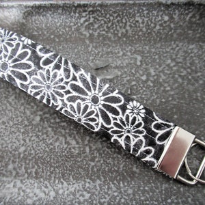 Op de afbeelding: Zwarte en witte bloemen sleutelhanger met een zilveren sleutelring.