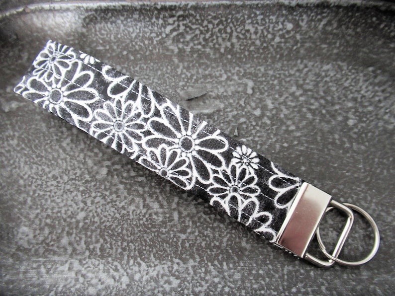Op de afbeelding: Zwarte en witte bloemen sleutelhanger met een zilveren sleutelring.