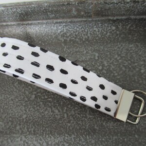 Op de afbeelding: Witte en zwarte sleutelhanger met een zwart-wit abstract patroon. De sleutelhanger heeft een zilveren metalen ring.