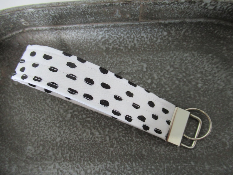 Op de afbeelding: Witte en zwarte sleutelhanger met een zwart-wit abstract patroon. De sleutelhanger heeft een zilveren metalen ring.