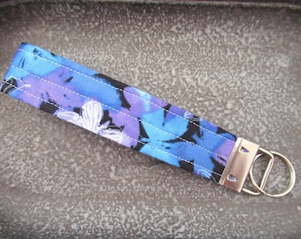 May include: A blue and purple floral patterned fabric key chain with a silver key ring.